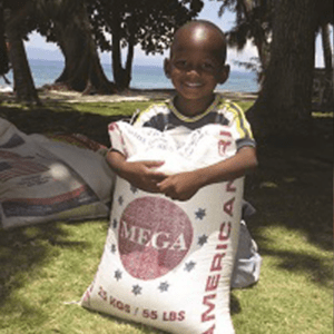 A young boy holding a bag of Rice for Christmas Fund in front of a beach.