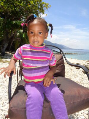 A little girl sitting on a chair on the beach.