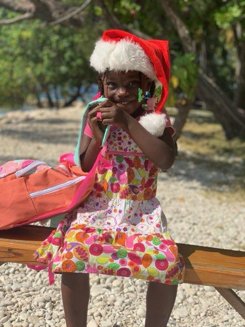 A young girl in a santa hat sitting on a bench.