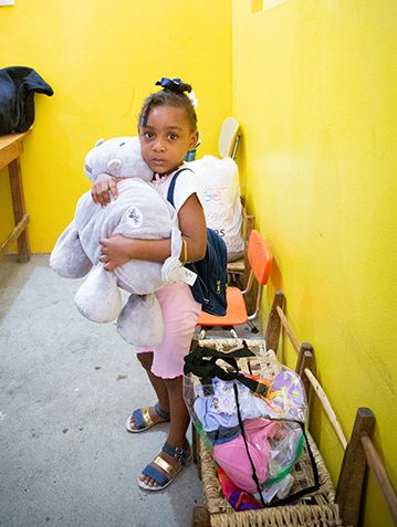 A young girl holding Backpacks and School Supplies.