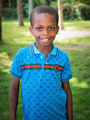 A young boy in a Francky Jean shirt standing in a park.