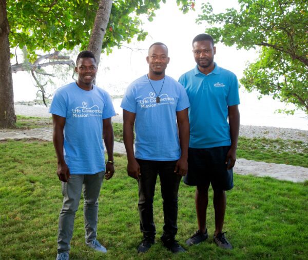 Three men in blue shirts standing in front of a tree.