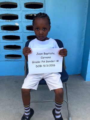A young boy sitting in a chair holding a sign.