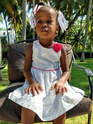 A little girl in a white dress sitting on a chair.