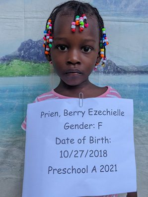 A little girl holding a sign that says date of birth preschool a 2021.