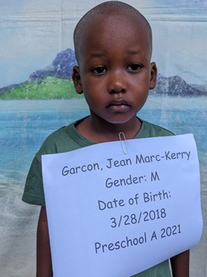 A young boy holding up a sign that says jean-marie kerry.
