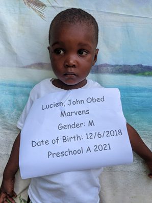 A young boy holding a sign that reads lucius john odd.