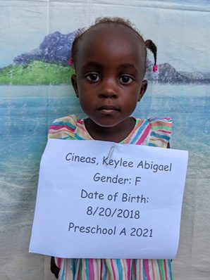 A little girl holding up a sign that says gender f date of birth 2021.