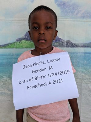 A young boy holding up a sign that reads jean pierre luxery genda.