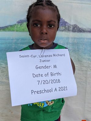 A young girl holding up a sign that says gender m date of birth preschool a 2021.