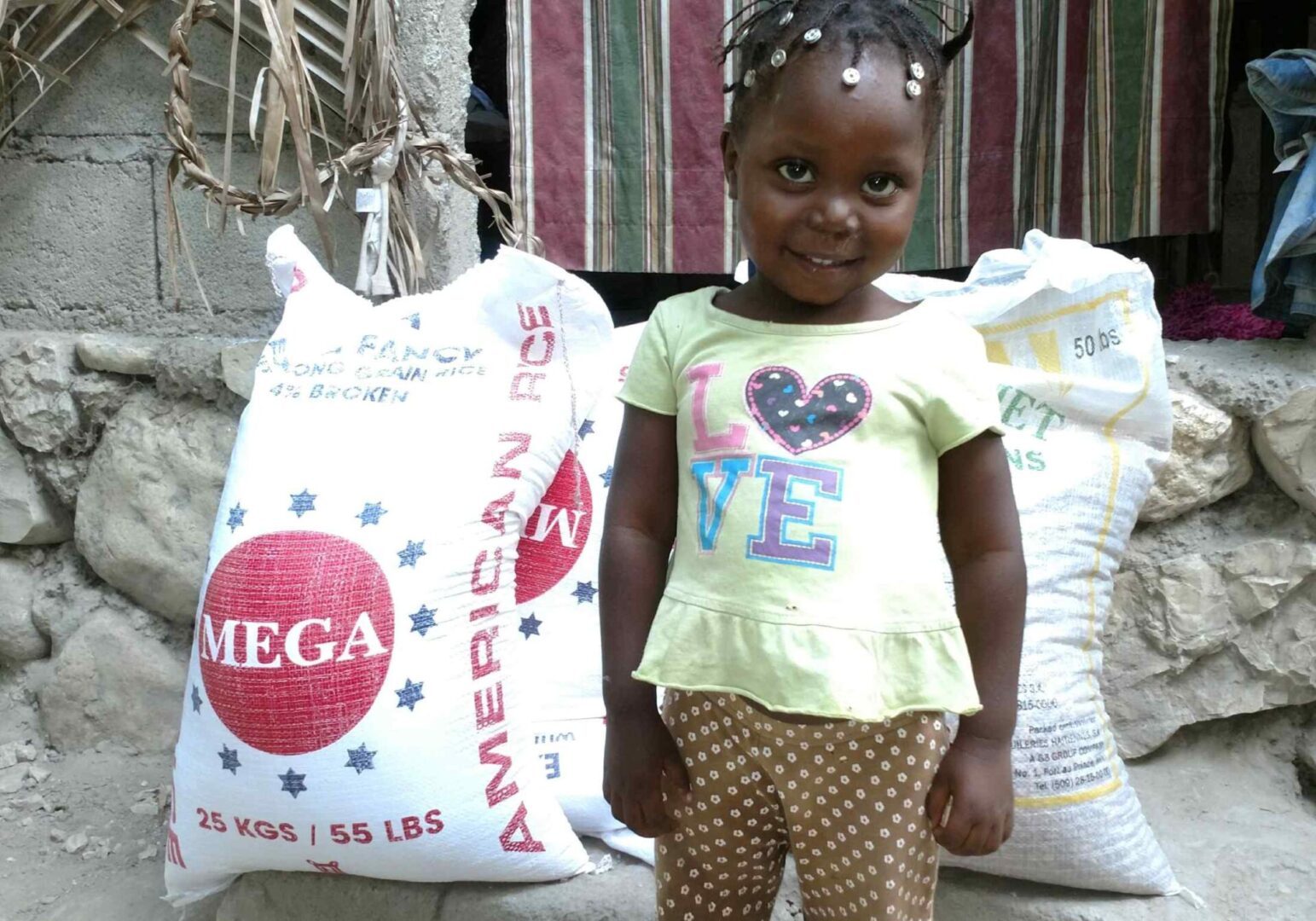 A young girl standing next to a bag of rice.