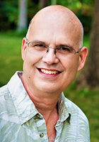 A bald man wearing glasses and a hawaiian shirt.